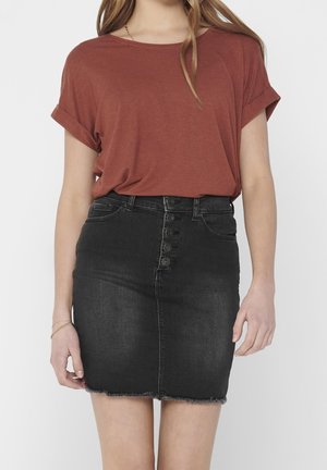 Vrouw draagt een roestkleurige top met korte mouwen, ingestopt in een hoge taille zwarte denim mini-rok met knopen aan de voorkant.