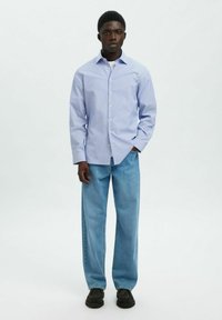 Lichtblauw overhemd met verticale strepen, gecombineerd met losse licht denim jeans en zwarte schoenen. Het overhemd heeft een kraag en lange mouwen.