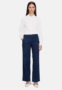 Hvid skjorte med krave og mørkeblå brede jeans. Skjorten har lange ærmer; jeansene har en tætsiddende talje og sidelommer. Hvide hæle.