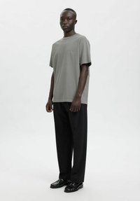 Helehall lühikeste varrukatega t-särk ümmarguse kaelusega, millele on lisatud laiad mustad püksid ja mustad mokassiinid, esitletud ühevärvilise tausta ees.