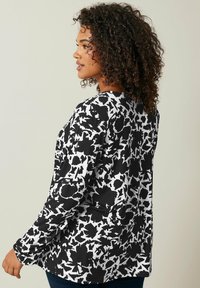Haut à manches longues en imprimé floral abstrait noir et blanc, avec un col rond et un tissu doux et lisse. Coupe décontractée avec une silhouette relaxée.