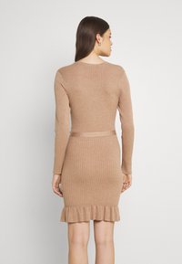 Abito lavorato a maglia color marrone chiaro con texture a coste, maniche lunghe, silhouette aderente e orlo a volant nella parte inferiore.