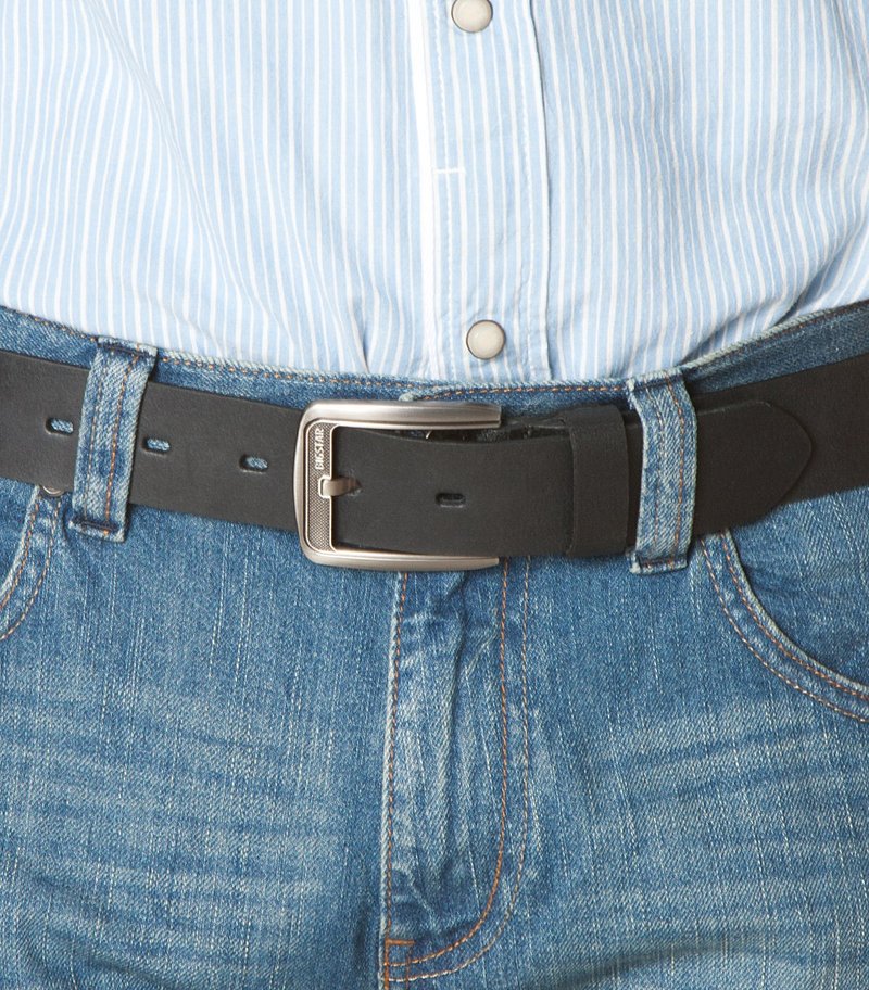 Fekete bőr öv ezüst színű fém csattal, sima textúrával és négy állítólyukkal, kék farmernadrággal viselve.
