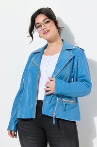 Blaue Leder-Motorradjacke mit silbernen Reißverschlüssen, Reverskragen und Seitentaschen. Darunter wird ein weißes Hemd und schwarze Jeans getragen.