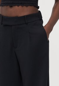 Black tailored trousers with a smooth texture, featuring side pockets, a mid-rise waistband, and a straight leg design.
