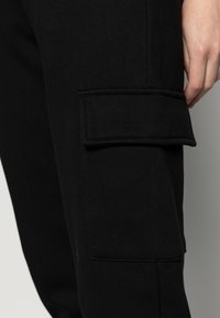 Svarta träningbyxor i en bomullsblandning med sidofickor. Tyget ser slätt ut med en mjuk textur och elastisk midja.