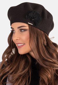 Sort strikket beret med en tekstureret blomsteraccent og en perlekant i midten. Har en sølvfarvet detalje på siden.