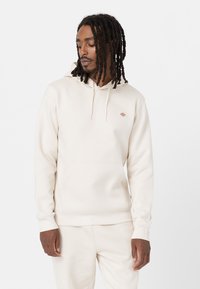 Cream hooded sweatshirt made of soft fabric, featuring a kangaroo pocket, ribbed cuffs, and a small logo on the chest.