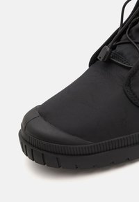 Chaussures noires avec une finition lisse et mate, dotées d'un bout rond. Semelle en caoutchouc épaisse avec des rainures texturées, équipée de lacets ajustables.