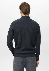Maglione grigio scuro lavorato a maglia con texture a coste, collo tondo e maniche lunghe, abbinato a jeans grigio scuro, visto da dietro.
