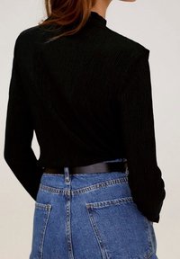 Maglietta nera a maniche lunghe con collo alto, abbinata a una gonna di jeans a vita alta con vita cintata e tasche posteriori visibili.