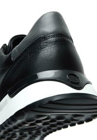 Sneaker in pelle nera con un design elegante, caratterizzato da una punta rotonda, suola bianca e dettagli neri lucidi sul tallone e ai lati.