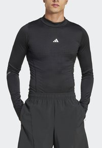 Langærmet sort atletisk skjorte med høj krave, der har et struktureret mønster og et hvidt Adidas-logo på brystet.