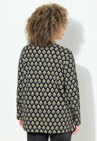 Schwarze Bluse mit langen Ärmeln und einem geometrischen Diagonal-Muster in Gelb und Weiß. Gefertigt aus weichem Material mit lässiger Passform.