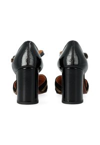 Chaussures à talons hauts noires avec une finition en vernis brillant, dotées d'un bout arrondi et de brides de cheville. Les talons sont larges et texturés.