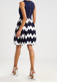Sjöblå och vit zigzag-mönstrad klänning med figurnära midja och utställd kjol, med en dragkedja i ryggen och matchad med sandaler med silverblockklack.