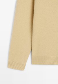 Beige knitted sweater featuring a round neckline and ribbed cuffs. Soft texture with a straight hem, suitable for casual wear.