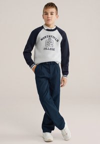 Sweat-shirt crème et marine avec le texte « NORTHFIELD COLLEGE » ; pantalon marine ; baskets blanches ; coupe décontractée ; poignets côtelés ; design casual.