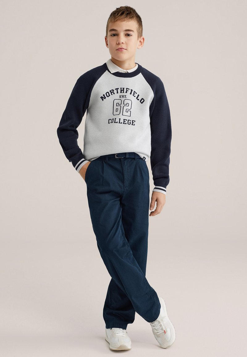 Sweat-shirt crème et marine avec le texte « NORTHFIELD COLLEGE » ; pantalon marine ; baskets blanches ; coupe décontractée ; poignets côtelés ; design casual.
