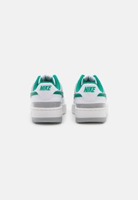 Sneakers bianchi Nike con dettagli verdi visti da dietro, con il logo Nike sulla linguetta del tallone su uno sfondo neutro.