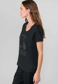 Sort kortærmet t-shirt med rund hals og et glitrende grafisk design på forsiden. Stoffet ser glat og blødt ud.