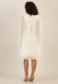 Abito lungo bianco con design di mantella fluente, dotato di una zip posteriore elegante e pieghe sottili. Tessuto morbido e leggero.