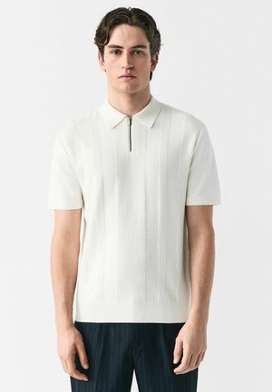 White short-sleeve polo shirt with a zippered collar, featuring textured vertical stripes and a ribbed hem. Paired with dark pinstripe trousers.