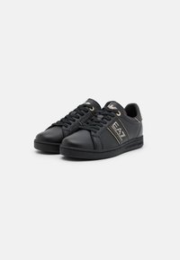 Svarta låga sneakers med perforerade sidor, guld EA7 Emporio Armani-logotyp på den yttre sidan, svarta snören och guldaccenter på tungan och h älen.
