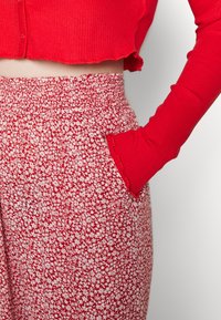 Red ribbed cropped sweater paired with high-waisted red floral pants featuring a white flower pattern and side pocket detail.