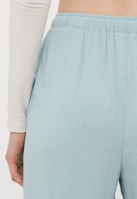 Světle modré, strukturované kalhoty s elastickým pasem. Design zahrnuje volný střih a boční kapsy pro funkčnost.