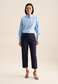 Camicia azzurro chiaro con colletto, abbinata a pantaloni cropped a vita alta color navy e tacchi a spillo neri. Texture lisce.