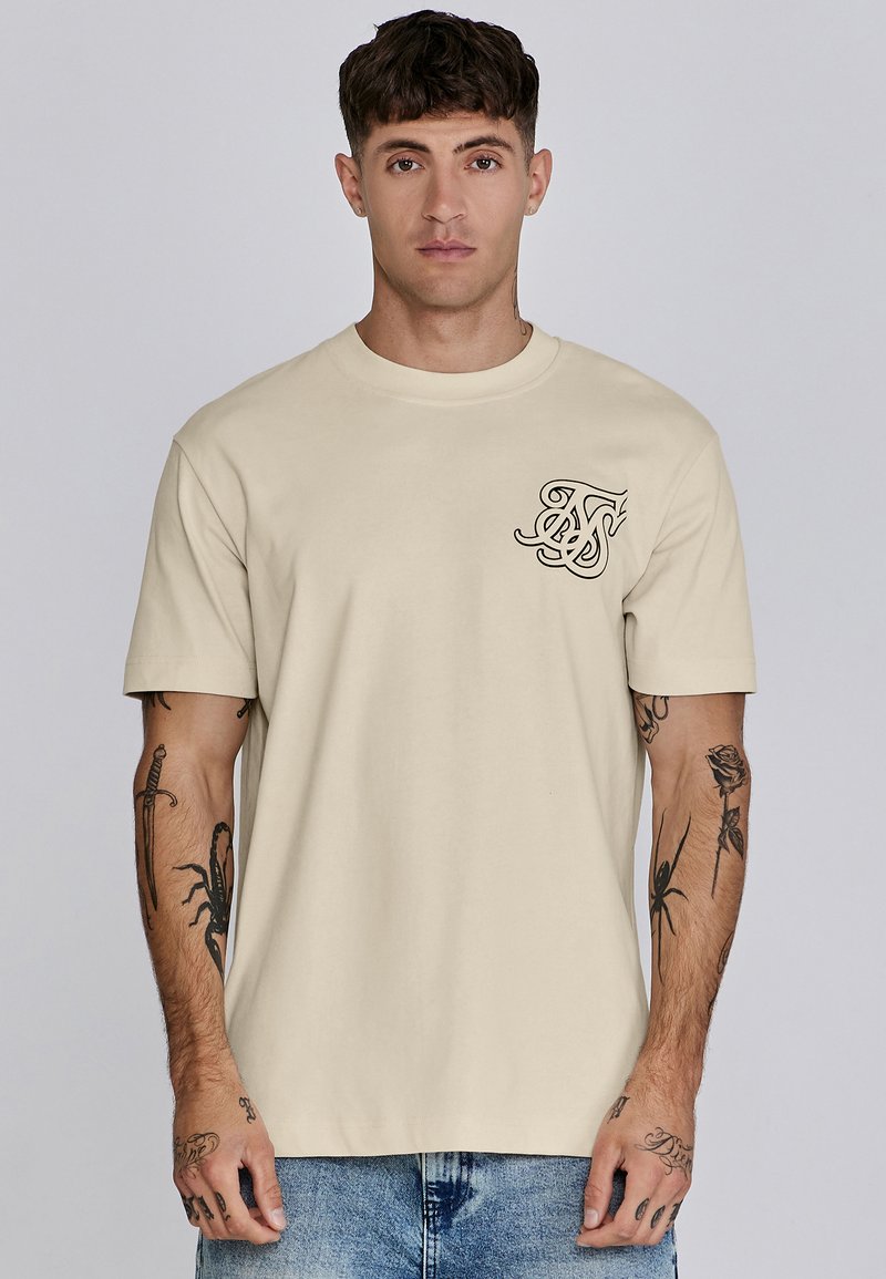 Beige Baumwoll-T-Shirt mit einem kleinen schwarzen Grafik auf der linken Brust. Kurze Ärmel und runder Halsausschnitt. Weiche Textur und lockere Passform.