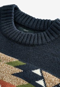 Granatowy sweter dzianinowy z prążkowanym dekoltem, z geometrycznym wzorem w odcieniach beżu, zieleni i bieli. Wykonany z teksturowanej przędzy. Widoczna metka marki.