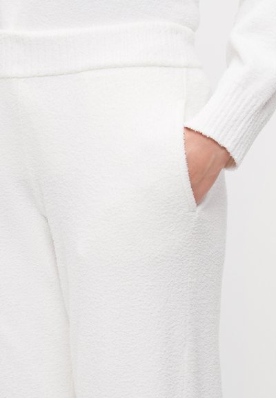 White fleece joggers featuring a textured surface, elastic waistband, and side pockets. Ribbed detailing at the cuffs.