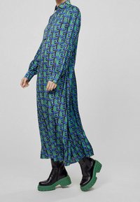 Tryckt långärmad klänning med ett geometriskt mönster i grönt och blått, kombinerad med kraftiga svarta stövlar med gröna sulor.