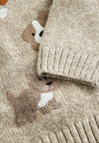 Pull en tricot beige clair avec des motifs de chiens brodés en brun et crème. Manches à bords côtelés et tissu texturé avec une finition douce.