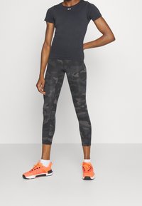T-shirt nero attillato, leggings a fantasia camouflage in tonalità di grigio e scarpe da ginnastica arancioni brillanti con dettagli neri.