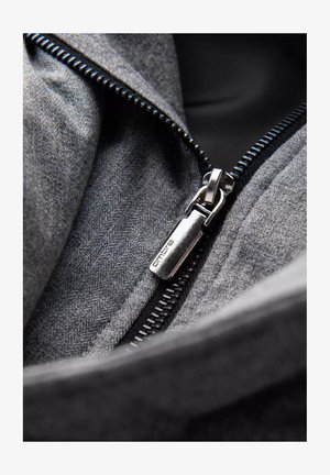 Interno in tessuto grigio con una cerniera nera. Rendiconto della cerniera contrassegnato con "omore". Il materiale presenta un sottile motivo a spina di pesce e una texture liscia.