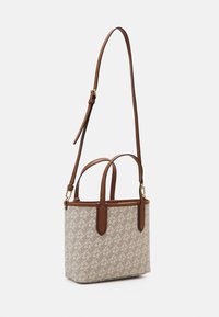 Pieni beige olkalaukku, jossa on ruskeat nahkakahvat ja säädettävä olkahihna, jossa on toistuva logo-kuvio.