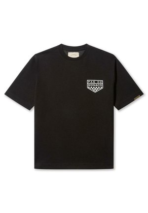Camiseta negra de manga corta en tejido de algodón, con un logo blanco "Pas de Monaco" y un patrón de tablero de ajedrez en el área del pecho izquierdo.
