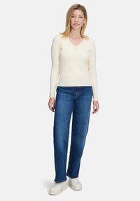 Hellbeige gerippter Pullover mit V-Ausschnitt, kombiniert mit blauen geraden Jeans und weißen Sneakers. Sauberes, lässiges Design.