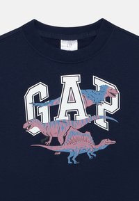 Navy Sweatshirt mit einem Grafikdesign von drei bunten Dinosauriern unter großen weißen "GAP" Buchstaben. Hergestellt aus weichem Baumwollgewebe.
