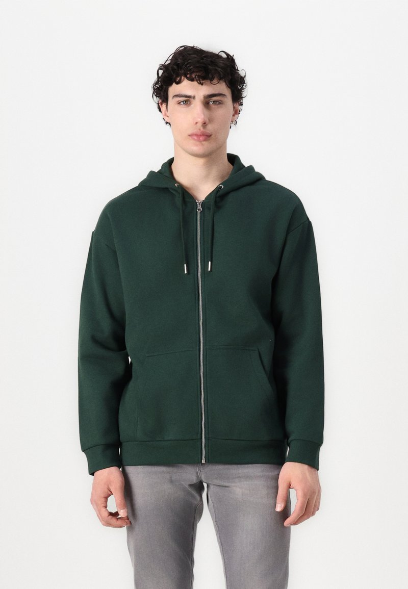 Hoodie zippé vert foncé avec une poche avant, capuche à cordon et poignets côtelés. Fabriqué à partir d'un tissu doux et texturé.