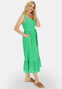 Zielona midi sukienka z dopasowanym topem, szerokimi ramiączkami i falbaniastym dołem. Posiada przewiązywany pasek oraz kieszenie, a całość zdobią małe czarne kropki.