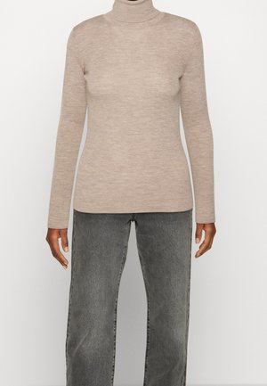 Pull à col roulé côtelé beige porté avec un jean noir délavé taille haute et jambes droites sur une personne à la peau foncée.