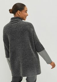 Szary, oversize sweter z wysokim kołnierzem i długimi rękawami, z czarno-białym paskiem na mankietach, wykonany z miękkiego, teksturowanego materiału.