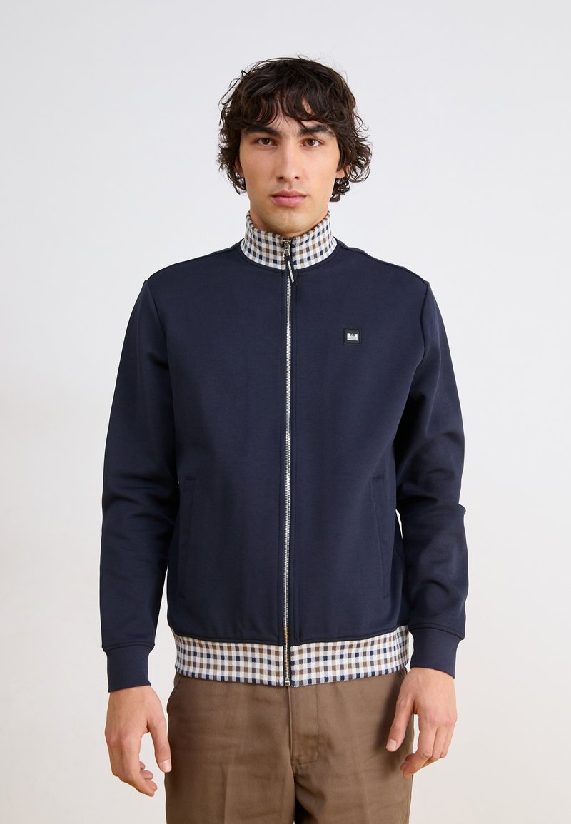 Navy zip-up jacket with a checkered collar and waistband. Features side pockets and a small logo on the chest. Smooth fabric texture.