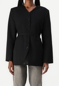 Černý blejzr s výstřihem do V a dlouhými rukávy, s vypasovaným pasem, šesti předními knoflíky a bočními kapsami. Hladká, strukturovaná tkanina.