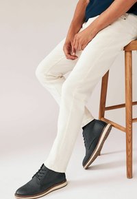 Pantalones blancos ajustados combinados con botas de cuero oscuras hasta el tobillo, con una suela blanca. Textura suave, diseño sencillo y sin patrones visibles.
