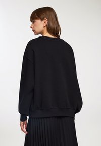 Czarny sweter z luźnym krojem, szerokimi rękawami i ściągaczem u dołu. Gładki materiał bez wzorów czy zdobień.